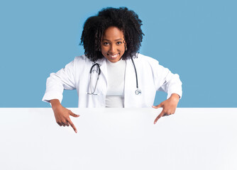 Happy black millennial lady doctor in white coat point fingers down at big banner with free space