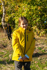 Caucasian girl in a yellow jacket on the background of the autumn forest. smiling and looking at the camera. In the background a boy with a bouquet of flowers