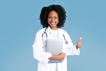 Happy black millennial lady doctor in white coat with tablet show thumb up