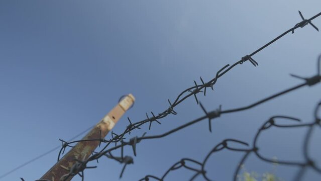 Old rusty barbed wire stretching on fence with metal poles outside. Security and crime concept.