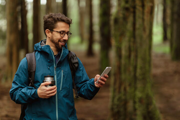 Positive young caucasian couple in jackets with cup of coffee, walk in forest together, enjoy trip,...