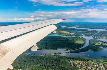 Fototapeta premium View of airplane wing, blue skies and green land and river during landing. Airplane window view.