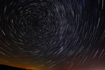 Circular star trails in the sky with a tint of city light from far away on the horizone