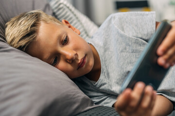 Cauacsian boy laying in bed and using a mobile phone. © cherryandbees
