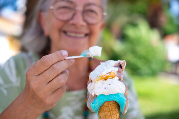 Blurred smiling senior woman eating a melting ice cream cone. Elderly caucasian grandmother enjoying sweet food and vacation in summer afternoon