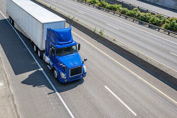 Blue day cab big rig semi truck with roof spoiler transporting cargo in dry van semi trailer...