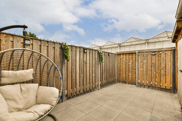 a patio with a hanging chair and wooden fenced in area next to the house, on a cloudy blue sky day