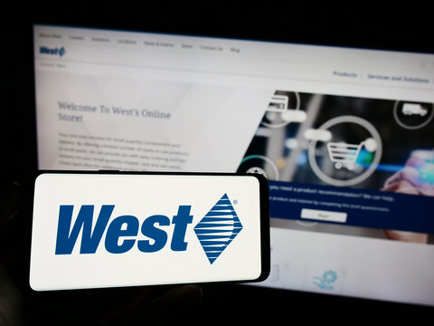 Stuttgart, Germany - 08-12-2023: Person holding mobile phone with logo of US company West Pharmaceutical Services Inc. on screen in front of web page. Focus on phone display.