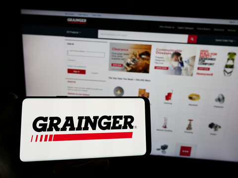 Stuttgart, Germany - 08-12-2023: Person holding mobile phone with logo of US industrial supply company W.W. Grainger Inc. on screen in front of web page. Focus on phone display.