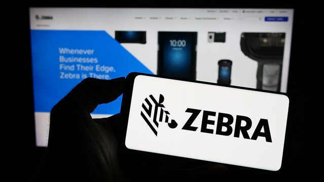 Stuttgart, Germany - 08-13-2023: Person holding smartphone with logo of US company Zebra Technologies Corporation on screen in front of website. Focus on phone display.
