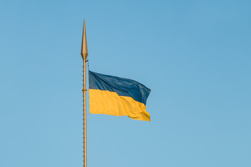 The national flag of Ukraine flutters in the wind on a high flagpole in the rays of sunset