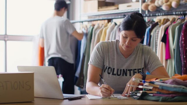 Male and female charity workers sorting through donations of clothing to thrift store - shot in slow motion