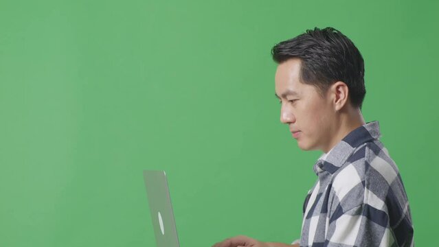Side View Close Up Of Asian Man Using Laptop Computer While Walking On The Green Screen Studio
