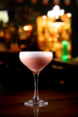 cocktail glass with creamy white foam and red berries orange peel garnish isolated on black background pub blurred background