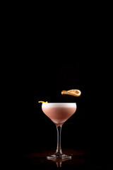 Dehydrated orange falling into milky berry cocktail glass isolated on black background