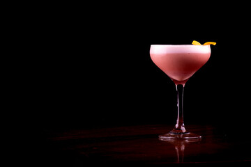 cocktail glass with white foam and berries with orange peel topping isolated on black background.