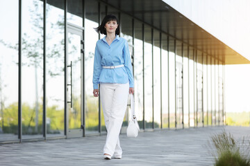 Relaxing and confident young business woman or entrepreneur walks by the modern office building company outdoors. Successful female career. Business people lifestyle, copy space.