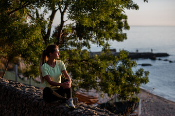 Fitness athlete runner woman relaxing in sunset. Girl sits on rocks after an active jogging workout.