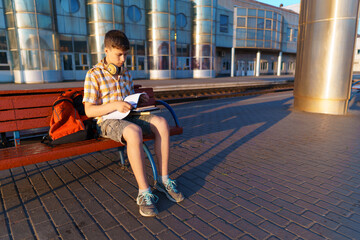 a student poses at a railway station, a boy is waiting for a train on the platform, reading books and doing homework, goes to study, the concept of education