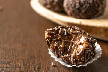 bitten brazilian brigadeiro (brigadier) with chocolate sprinkles on a wooden spoon over wooden table. traditional brazilian candy for party dessert