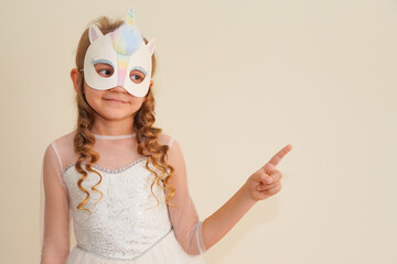 Unique child.  A girl in a carnival masquerade unicorn mask made by her own hands points her finger at an empty place.