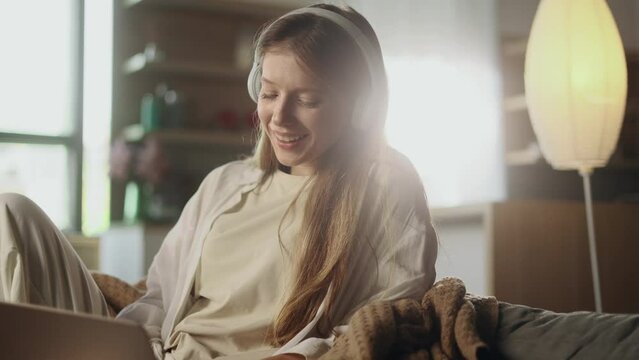 Pretty young woman freelancer with headphones listening music while working online typing browsing on laptop and singing indoors Positive female enjoying great working day at cozy home