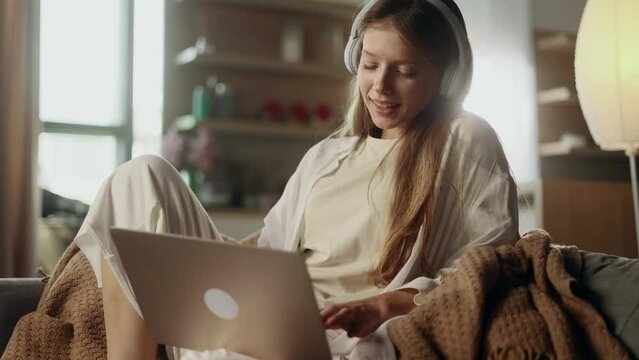 Pretty young woman freelancer with headphones listening music while working online typing browsing on laptop and singing indoors Positive female enjoying great working day at cozy home