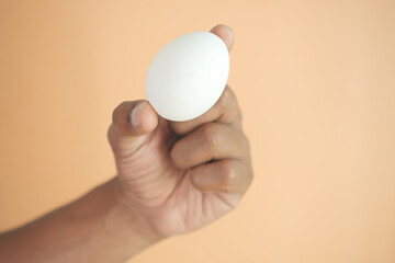 men holding a white egg against orange color background 