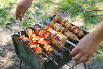 Grilled pieces of meat on skewers, shish kebab with vegetables, cooking process on fire, on brazier. Roasted marinated meat cooked at barbecue, picnic in summer day.
