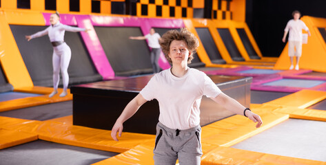 Smiling young guy in white t-shirt and gray sweatpants having great time while jumping on trampoline in game club