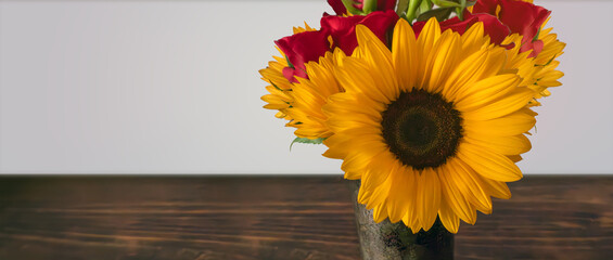 Sunflower and roses on a vase on a wooden table