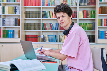 Young male student sitting with laptop with books in college library