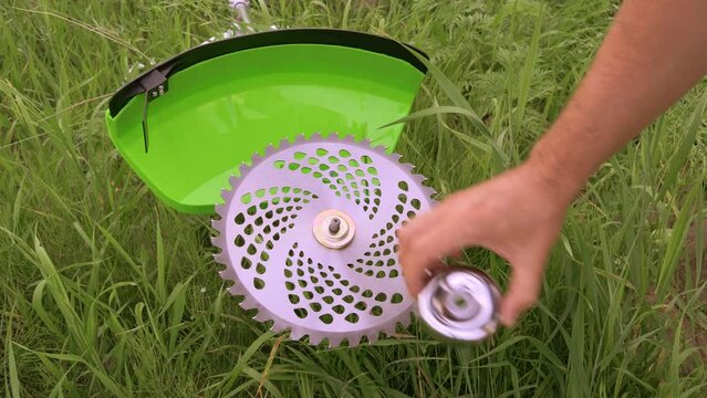 Installing a saw blade on a new green brush cutter. Gardener sets up a saw blade against a grassy field, close up. Preparing the brush cutter for work. Servicing garden tools.