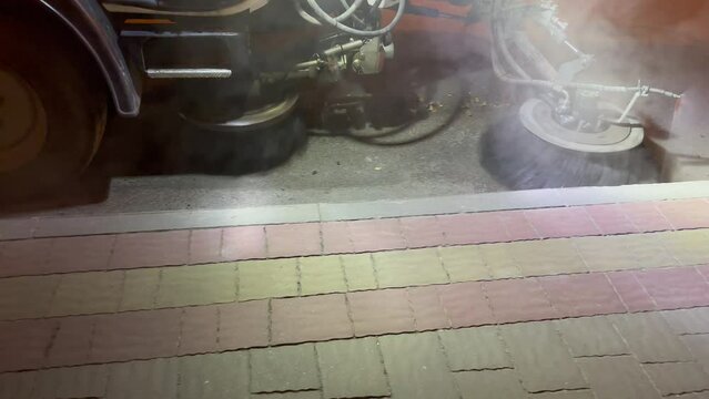 A street-cleaning machine works on a road with a lot of dust. The sweeper is working. A special machine (sweeping machine) sweeps the streets with a special brush