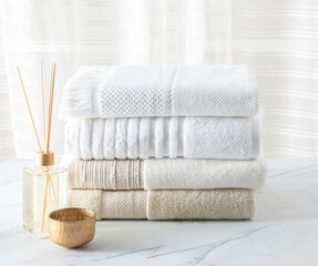 White cotton bath towels folded and aroma diffuser on a white marble table in the bathroom. Neutral...