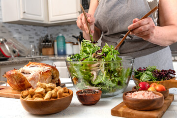 female hands make caesar salad with vegetables and chicken in the home kitchen. Croutons, chicken and salt in the foreground.