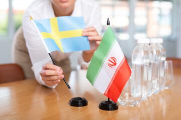 Little flag of Iran on table with bottles of water and flag of Sweden put next to it by positive...