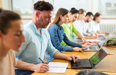 Fototapeta premium Man sitting in classroom during lecture in university and using laptop.