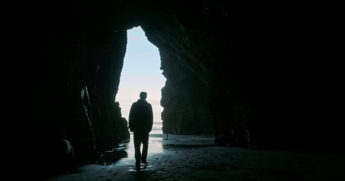 Aerial: Man walking out of a cave into the light. 