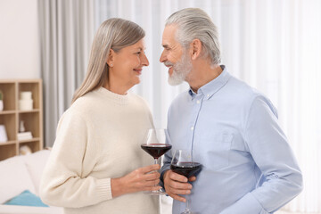 Affectionate senior couple with glasses of wine indoors