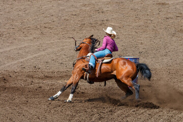 Cowgirl riding in a barrel racing completion at a rodeo. She is wearing red shirt and blue jeans...