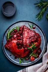 Baked duck legs in wine and cherry sauce with rosemary. Gourmet dinner with red wine glass. Blue stone table background, top view