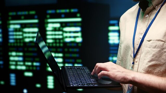 Developer doing yearly system upkeep, imputing data on laptop of required fixing in supercomputers housing advanced data storage hardware supporting important IT workloads