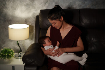 happy mother breastfeeding infant baby on sofa in the living room at night