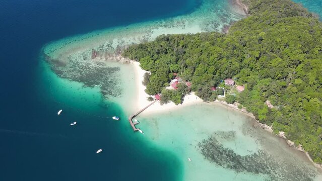 Aerial Overhead View Of Sapi Island On Clear Sunny Day With Pier and Resort Buildings Seen Below. Push Forward Shot