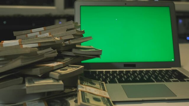 A lot money packs 100 hundred American dollar bills folded pyramid on table with laptop chromakey in office evening on background, close up.