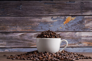 Coffee beans in a red coffee cup and many coffee beans placed around on a wooden table in a warm, light atmosphere, on a dark background, with copy space.