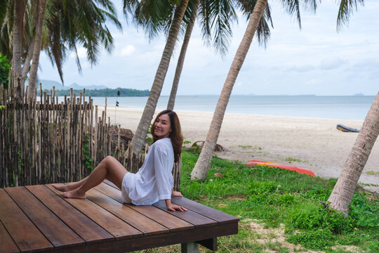 Portrait image of a beautiful young asian woman sitting on wooden balcony by the sea