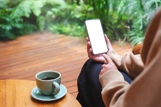Mockup image of a woman holding mobile phone with blank white desktop screen in the garden