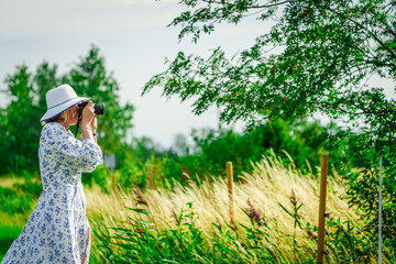 Side view of calm young female traveler in casual summer clothes taking photo of nature. Woman is a professional photographer with dslr camera, outdoor.